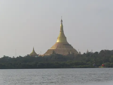 The golden Global Vipassana Pagoda rising above trees, seen across the water
