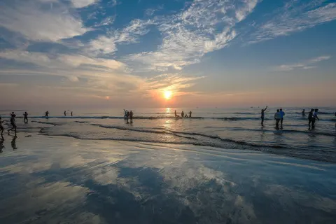 Low sun over Juhu Beach, wet sand mirroring the sky as people wade in the shallows