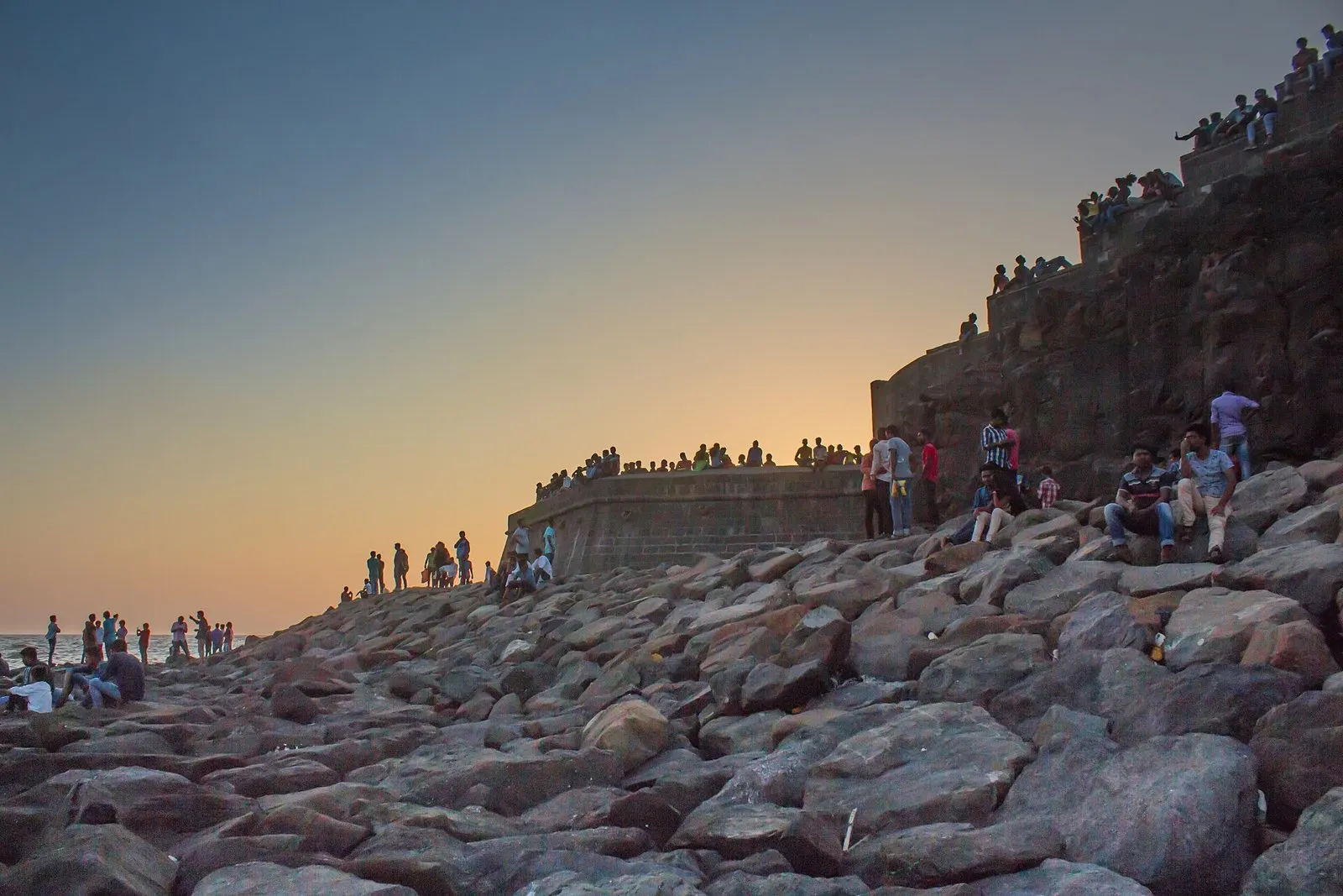 Bandra Fort’s stone walls rising above the rocks at sunset, people along the ramparts