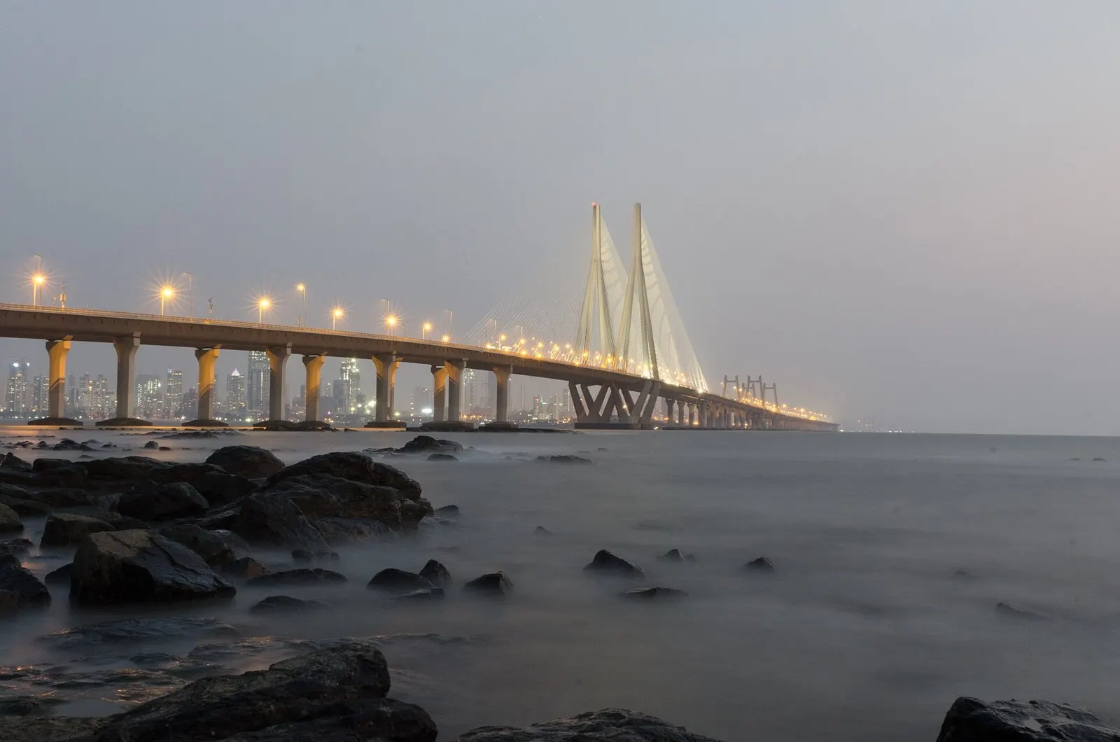 The Bandra–Worli Sea Link lit up at dusk, seen across the rocks from Bandstand