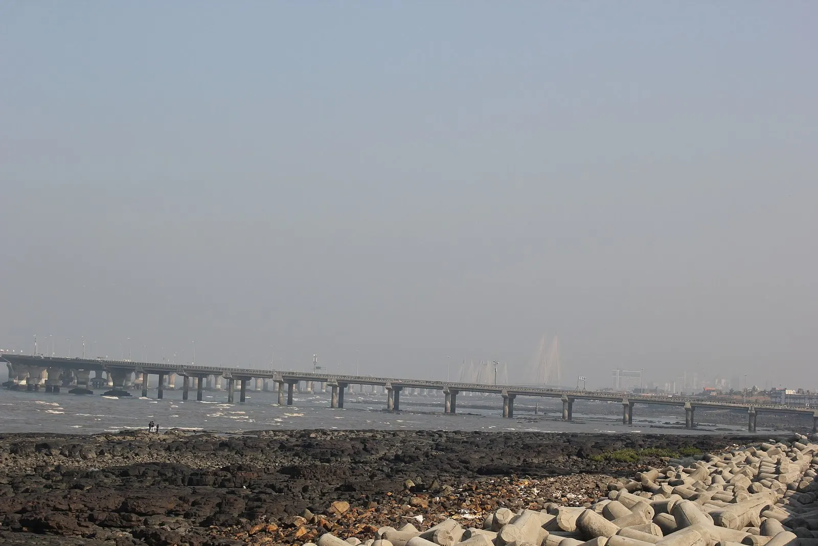 Hazy view of the Sea Link beyond the tetrapods and rocks of Worli Sea Face