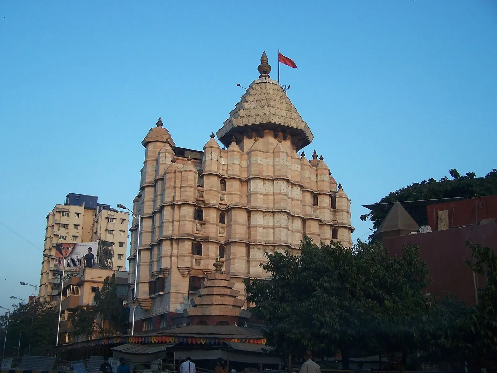 Siddhivinayak Temple’s pale stone tower and dome with a saffron flag against a clear blue sky