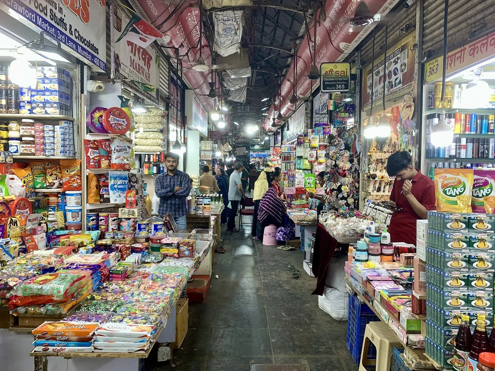 A covered lane of shops piled with sweets, spices and household goods inside the market